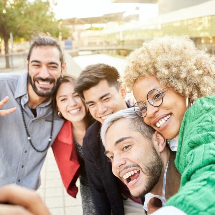 Group of cheerful friends taking smiling selfies outdoors